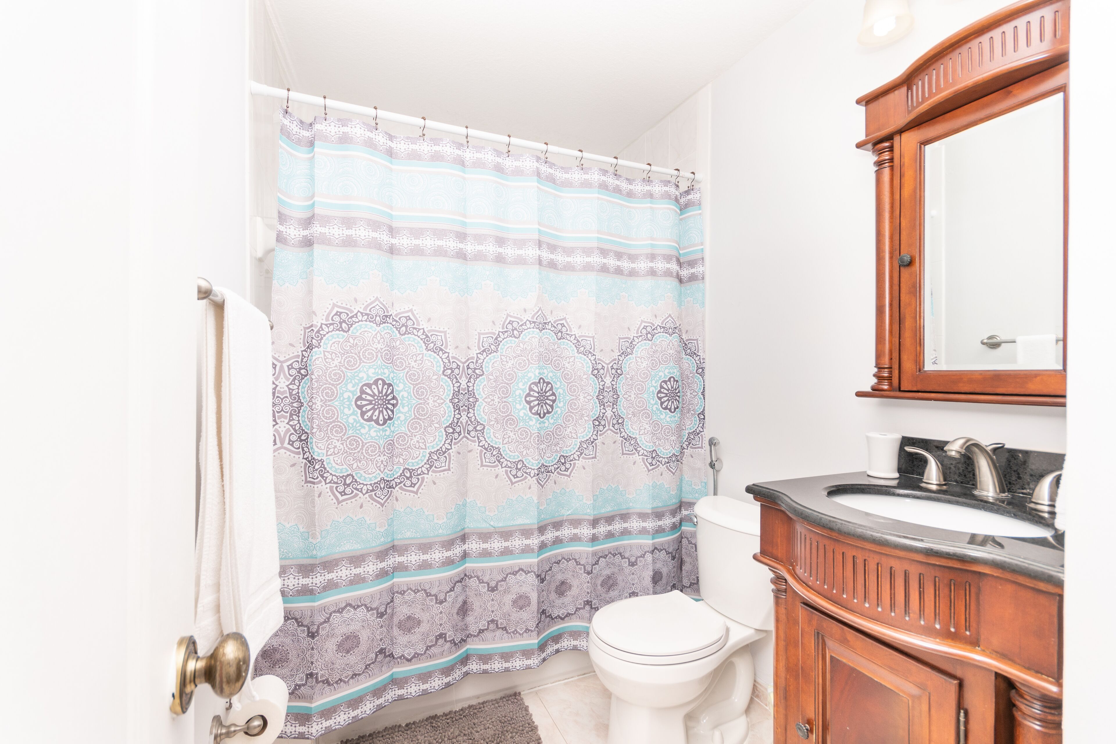 Un baño con cortina de ducha estampada, inodoro, lavabo con espejo y un mueble de madera.