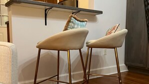 Una cocina con armarios de madera, una encimera y dos taburetes de bar con patas doradas.