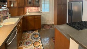 Una cocina con armarios de madera, un refrigerador de acero inoxidable, una estufa a gas y un tapete estampado.