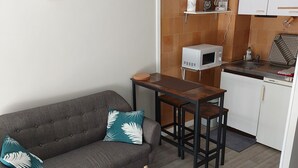 Ein kompakter Wohnbereich mit einer Couch, zwei kleinen Tischen, einer Küchenzeile inklusive Mikrowelle, Toaster und Spüle.