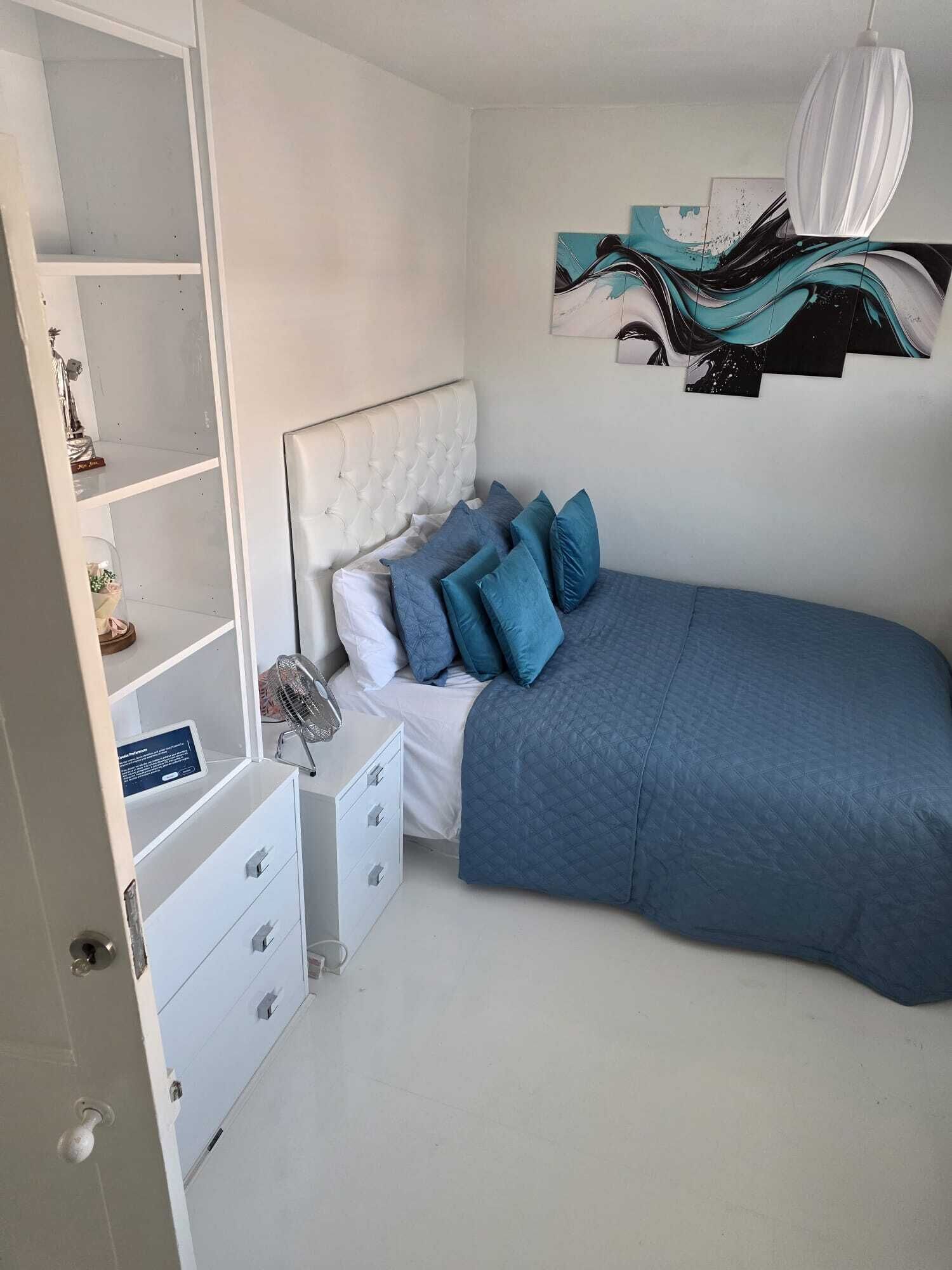 Ein Schlafzimmer mit einem Bett, einem Nachttisch, einem Wandbild und einer Tür.