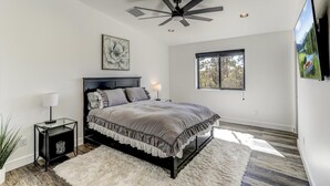 Ein Schlafzimmer mit Bett, Deckenventilator, Fenster, Nachttisch und Fernseher.