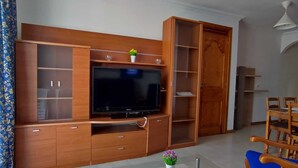 A living room with a large flat-screen TV, wooden cabinets, and a blue chair. - Suitable. Deep beach, a few meters from the beach. (Playa Honda)