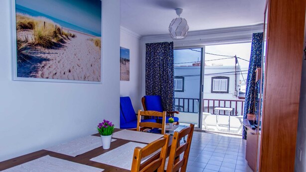 A dining area with a wooden table and chairs, a potted plant, and a beach-themed painting on the wall. - Suitable. Deep beach, a few meters from the beach. (Playa Honda)