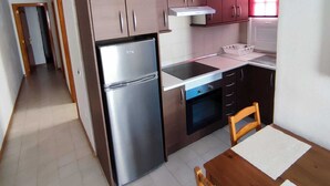 A compact kitchen with a refrigerator, stove, oven, and wooden cabinets. - Suitable. Deep beach, a few meters from the beach. (Playa Honda)