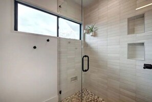 A modern bathroom with a glass shower enclosure, white tiled walls, and a window above the shower. - Zilker Zen Sanctuary (Austin)