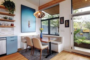 A modern kitchen with a dining area, wooden flooring, and a large window with a view of the outdoors. - Zilker Zen Sanctuary (Austin)