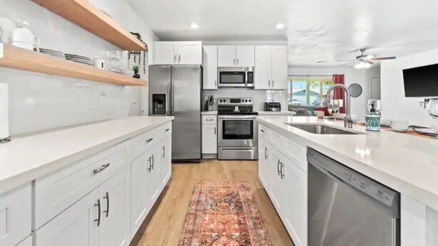 A modern kitchen with white cabinets, stainless steel appliances, and a wooden shelf. - Stunning Gilbert Home w/ Heated Pool and Hot Tub (Mesa)