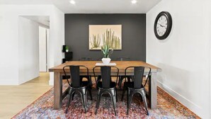 A dining area with a wooden table, black chairs, a cactus painting, and a clock on the wall. - Stunning Gilbert Home w/ Heated Pool and Hot Tub (Mesa)