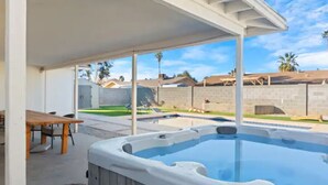 A hot tub in a covered outdoor area with a table and chairs nearby. - Stunning Gilbert Home w/ Heated Pool and Hot Tub (Mesa)