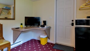 Ein kleines Zimmer mit Schreibtisch, Fernseher und einem kleinen Mülleimer.