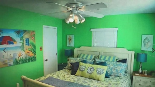 Ein Schlafzimmer mit einem Bett, einem Deckenventilator, einem Nachttisch und einem Wandbild.