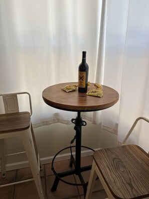 Une petite table ronde, une bouteille de vin, deux chaises et un rideau en arrière-plan.