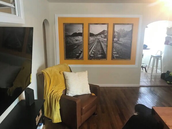 Un salon avec un canapé marron, un plaid jaune et un grand tableau représentant une voie ferrée, accroché au mur.