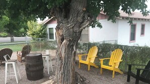 Un arbre avec un tronc imposant et un sol recouvert de gravier. On y trouve des chaises Adirondack jaunes et noires, ainsi qu’une chaise blanche.