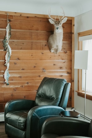 A room with a wooden wall, a mounted deer head, a leather chair, and a fish hanging on the wall. - Crazy View Beach Front Bay City, MI (Bay City)