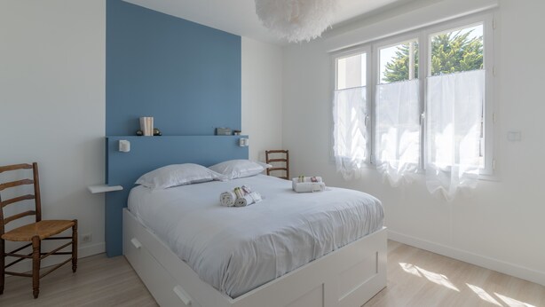 Una camera da letto con un letto, una sedia, un comodino, una finestra con tende e una lampada a soffitto.