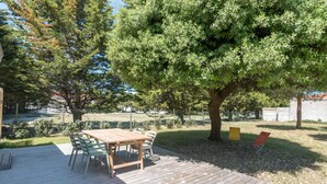 Un patio in legno con tavolo e sedie, immerso tra alberi e un prato.