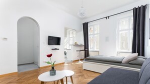Un salon moderne avec un canapé, une petite table sur laquelle est posé un vase, un téléviseur fixé au mur et une fenêtre avec des rideaux.