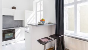 Une cuisine moderne avec des meubles blancs, un four encastré et une fenêtre avec des rideaux.