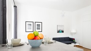 Un salon moderne avec un canapé gris, une table basse et un coin repas agrémenté d’un saladier de fruits et de verres.