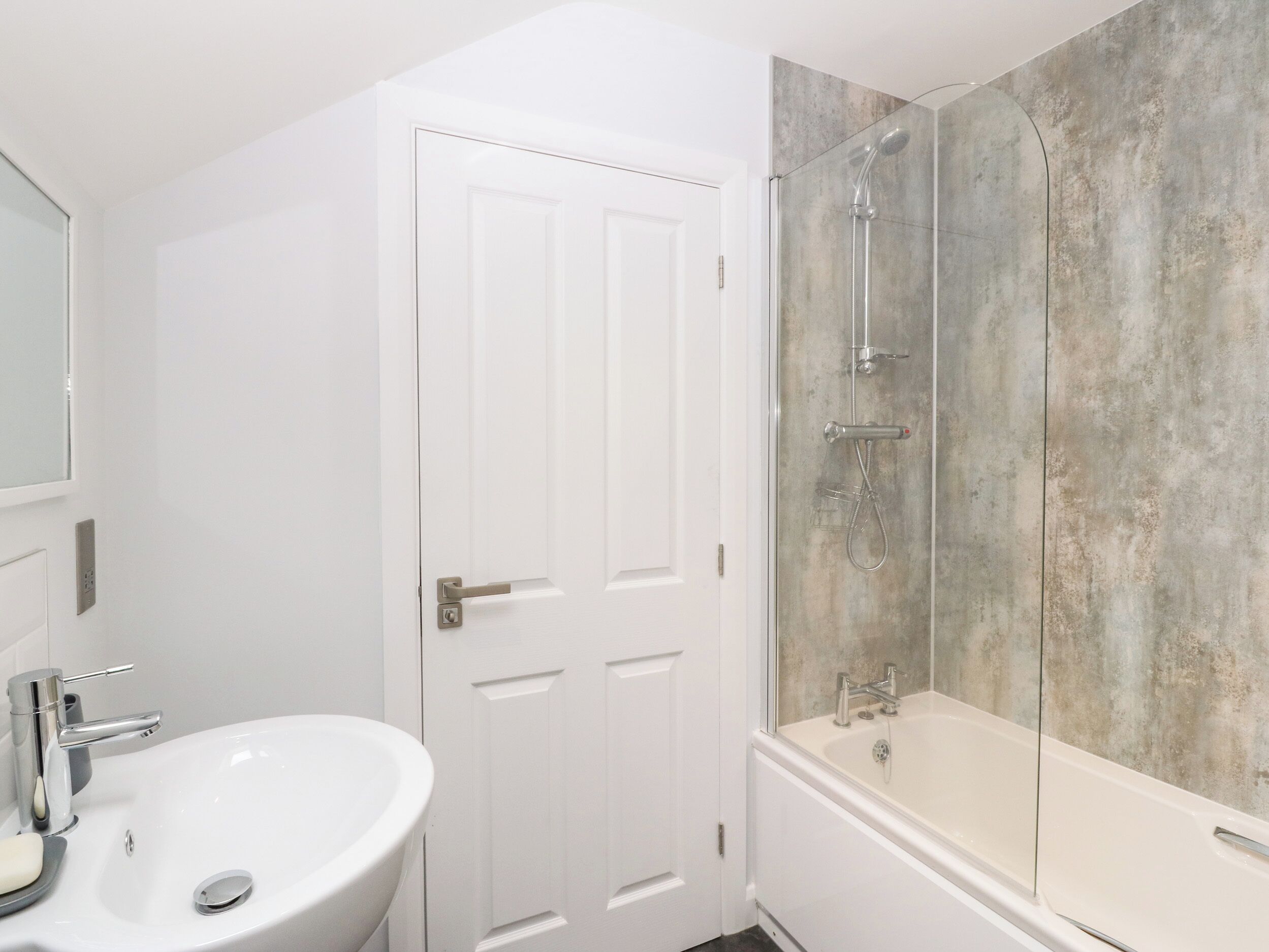 A bathroom with a white sink, a door, and a shower with a concrete wall.