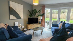 A living room with a TV, sofa, coffee table, and a plant. - 11 Parc Delfryn (Brynteg)