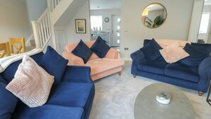 A living room with two sofas, one peach and one blue, both with dark cushions. There's a round coffee table in the center. - 11 Parc Delfryn (Brynteg)