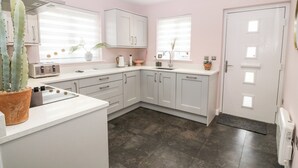 A modern kitchen with white cabinets, a built-in oven, and a large window. - 11 Parc Delfryn (Brynteg)