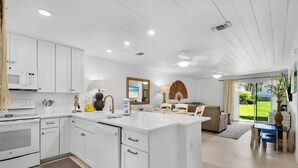 A modern kitchen with white cabinetry, a central island, and a dining area with a table and chairs. - Townhome with Gulf Access (Miramar Beach)