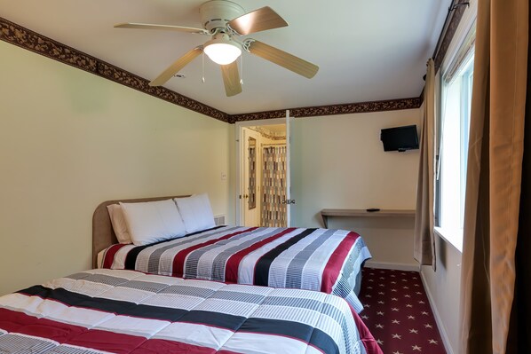 Ein Hotelzimmer mit Bett, Deckenventilator, Fernseher und einem Fenster mit Vorhängen.