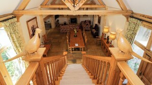 A spacious loft-style room with a high ceiling, wooden beams, a chandelier, a dining table, and a staircase leading to an upper level. - Rookery Hall (Broadway)