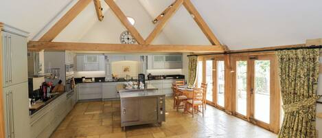 A spacious kitchen with a central island, wooden beams, and a large window with curtains.