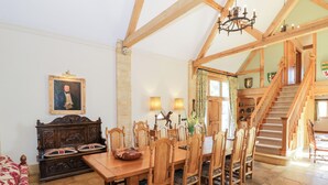A dining area with a wooden table and chairs, a sofa, and a staircase leading to an upper level. - Rookery Hall (Broadway)