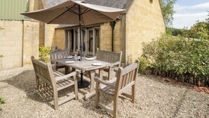 An outdoor dining area with a table and chairs, a large umbrella, and a stone building in the background. - Rookery Hall (Broadway)