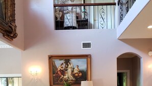 A spacious living room with a high ceiling, a grand staircase, and a large painting.