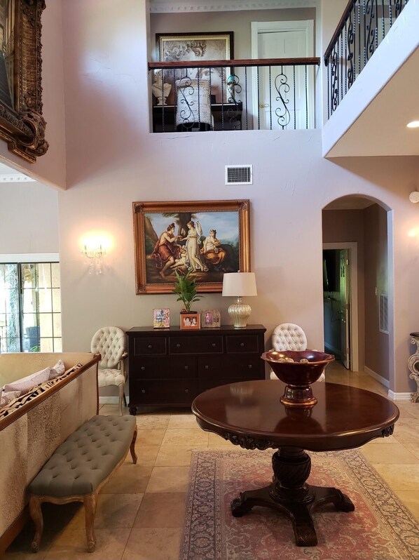A spacious living room with a high ceiling, a grand staircase, and a large painting.