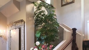 A grand staircase with a dark wooden handrail, a large mirror with ornate detailing, and a potted plant with flowers.
