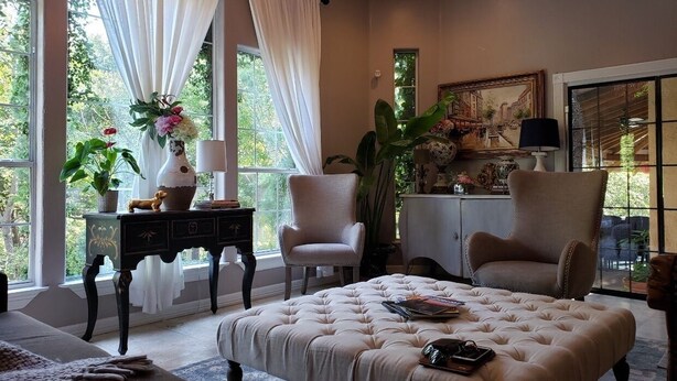 A well-lit room with a large window, a chandelier, and two armchairs.