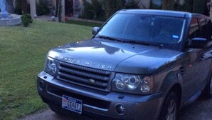 A Range Rover parked in front of a house with a red roof and a statue in the front yard.