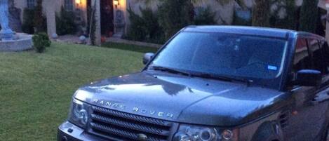 A Range Rover parked in front of a house with a red roof and a statue in the front yard.