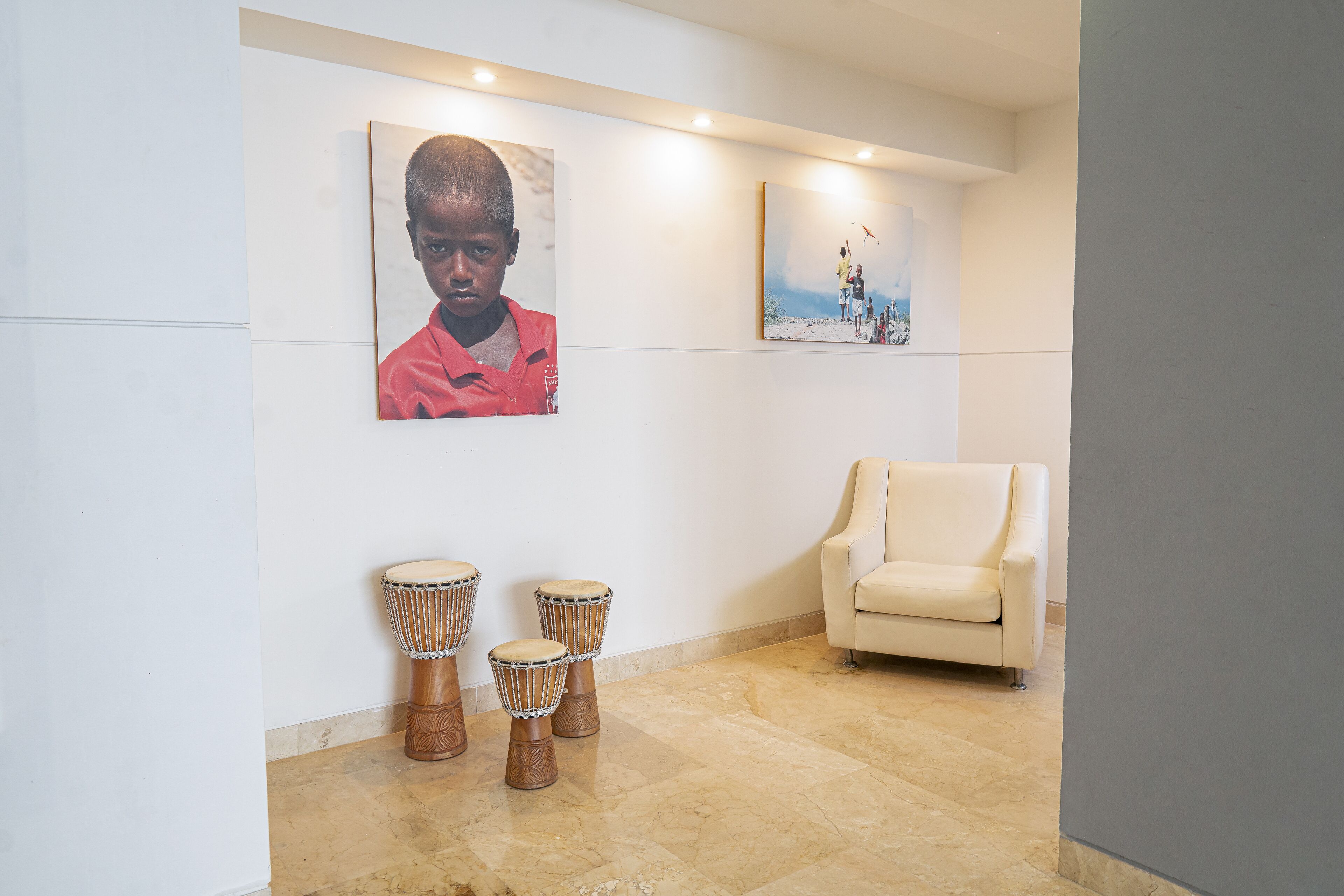 Una habitación con un sofá color beige, tres tambores djembe y dos cuadros en la pared.