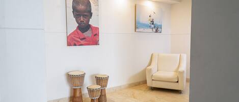 Una habitación con un sofá color beige, tres tambores djembe y dos cuadros en la pared.