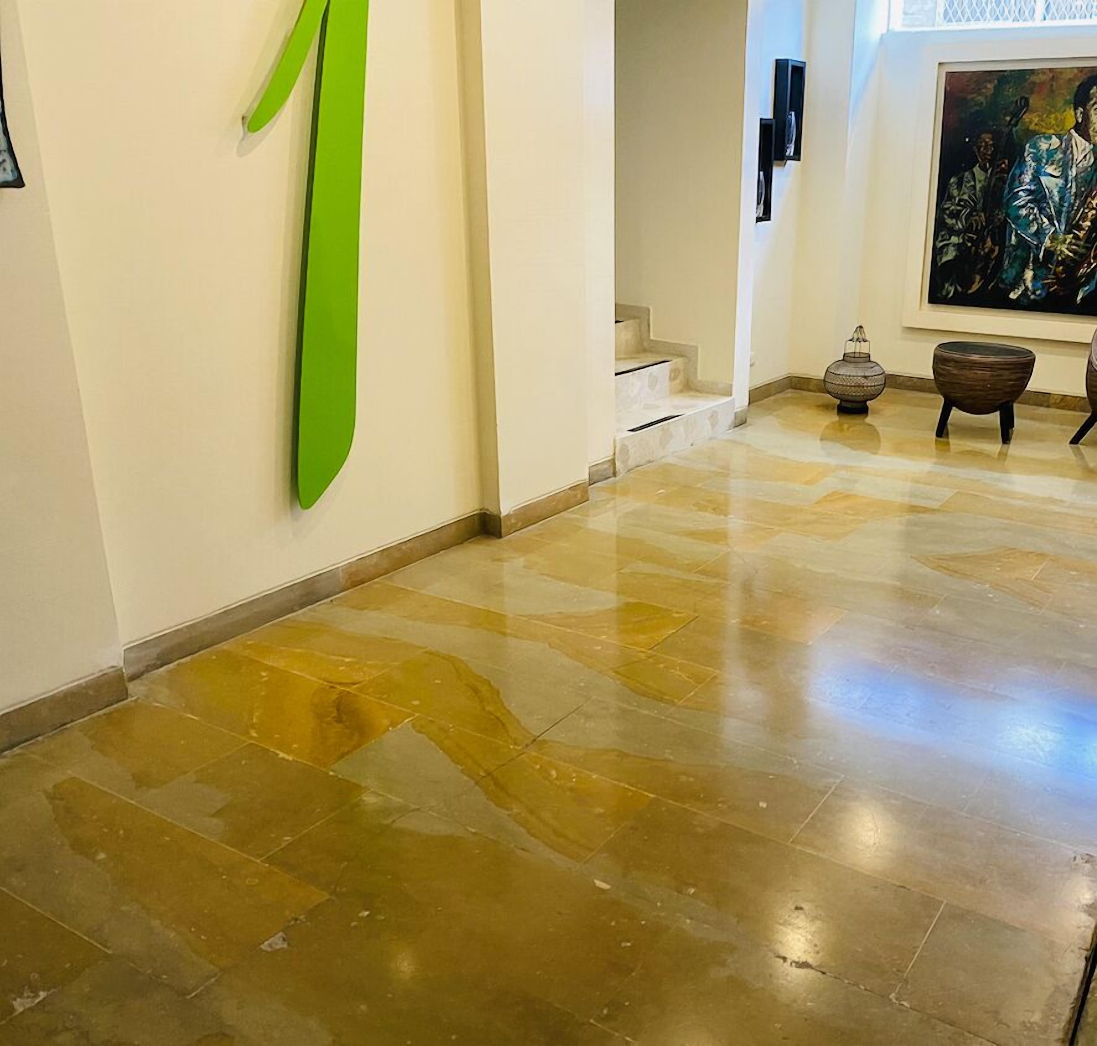 Un couloir doté d’un sol en pierre polie, d’une œuvre d’art abstraite verte ornant le mur et d’un escalier menant à un niveau supérieur.