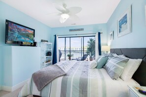 Ein Schlafzimmer mit Bett, Fernseher, Deckenventilator, Balkon und Blick ins Freie.