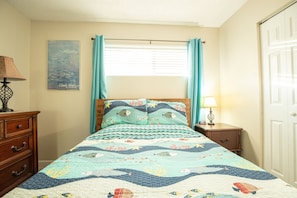 A bedroom with a bed, a nightstand, a dresser, a window with curtains, and a door.