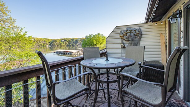 Une terrasse dotée d’une table ronde et de quatre chaises, offrant une vue sur un lac et des arbres.