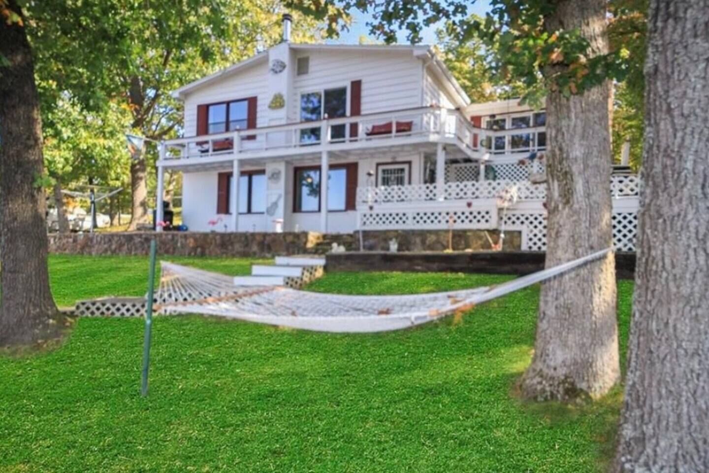 A two-story house with a balcony, surrounded by trees and a hammock.