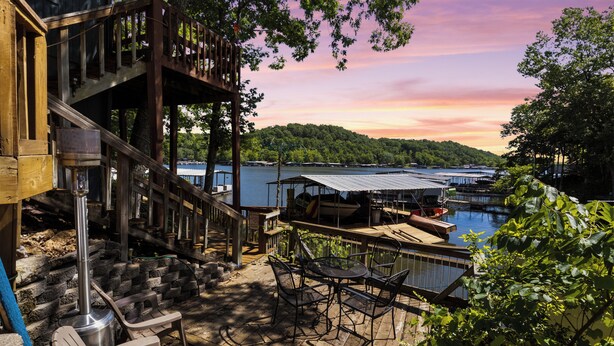 Une terrasse en bois avec des meubles d’extérieur, un barbecue en métal et une vue sur un lac et une zone de quai.