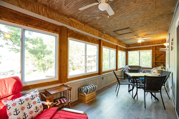 A room with wooden walls and ceiling, large windows, a dining table with chairs, a red sofa, and a ceiling fan. - Wonderful Remote Lake Cabin! Fish from Deck & Dock (Rocky Mount)